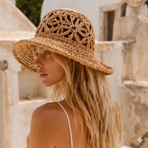 May include: A tan crochet bucket hat featuring a prominent openwork floral pattern across the crown and a wide, slightly downturned brim. The hat is constructed from a natural-toned woven fiber with a textured, hand-crafted appearance.