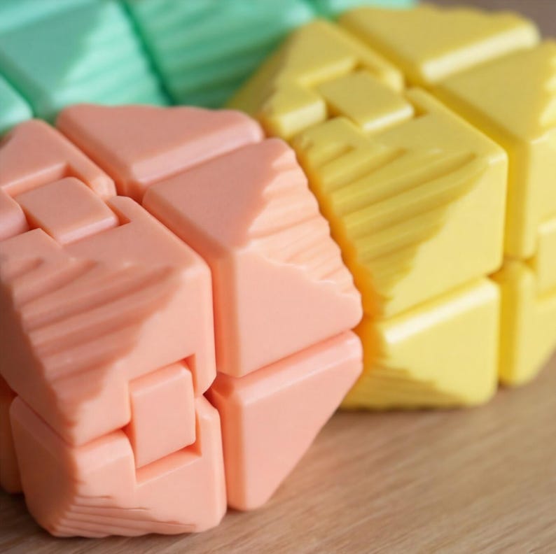 May include: Close-up of a colorful puzzle toy. The puzzle is composed of interlocking cube-shaped pieces in shades of peach, yellow, and green. Each piece has a textured surface with diagonal lines, creating a tactile and visually appealing design.