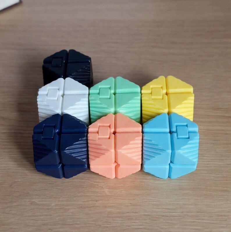 May include: A collection of colorful, geometric puzzle toys in various shades including black, white, green, yellow, navy blue, peach, and light blue. Each puzzle has a unique shape and design, with visible lines and textures.