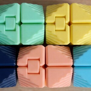 May include: Close-up of several colorful fidget toys. The toys are made of plastic and come in various colors, including green, yellow, peach, blue, and navy. Each toy is composed of four connected blocks with a textured surface.
