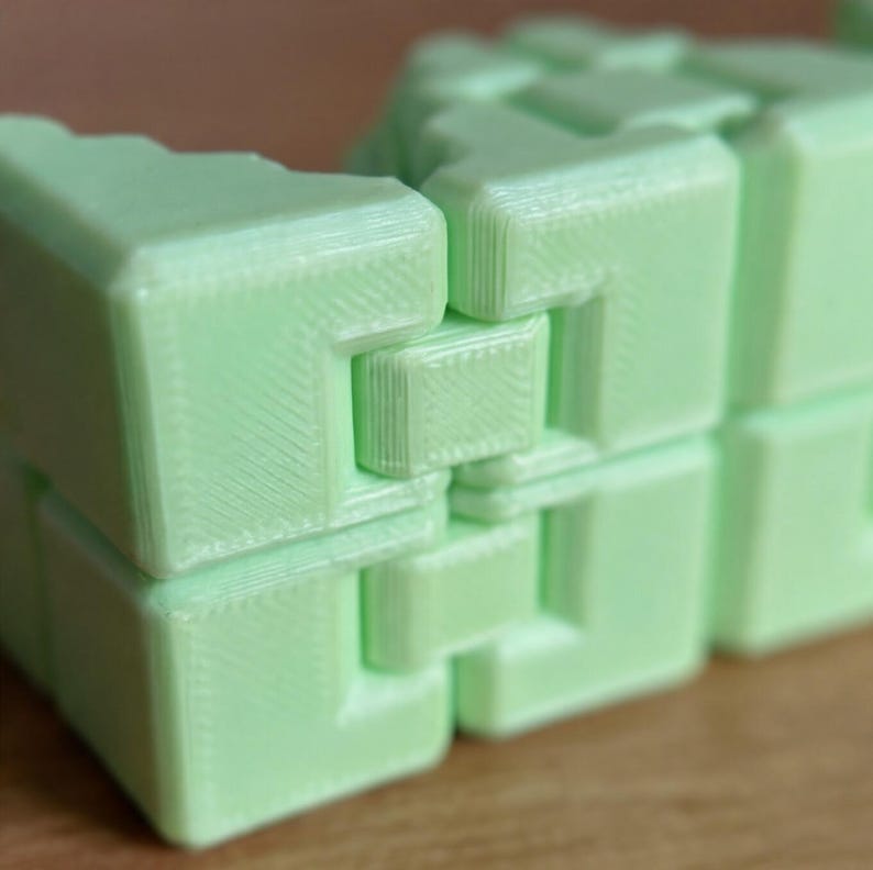May include: Close-up of a light green, interlocking puzzle. The puzzle is made of several connected, rectangular blocks with a textured surface. The blocks are arranged in a stacked formation, showcasing the interlocking design.