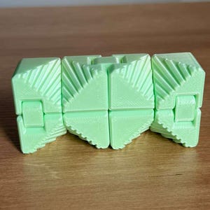 May include: A light green, geometric fidget toy with a segmented design. The toy is made of plastic and has a series of connected, triangular-shaped pieces. The pieces are hinged together, allowing the toy to be manipulated and reconfigured.