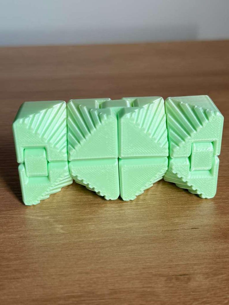 May include: A light green, geometric fidget toy with a segmented design. The toy is made of plastic and has a series of connected, triangular-shaped pieces. The pieces are hinged together, allowing the toy to be manipulated and reconfigured.