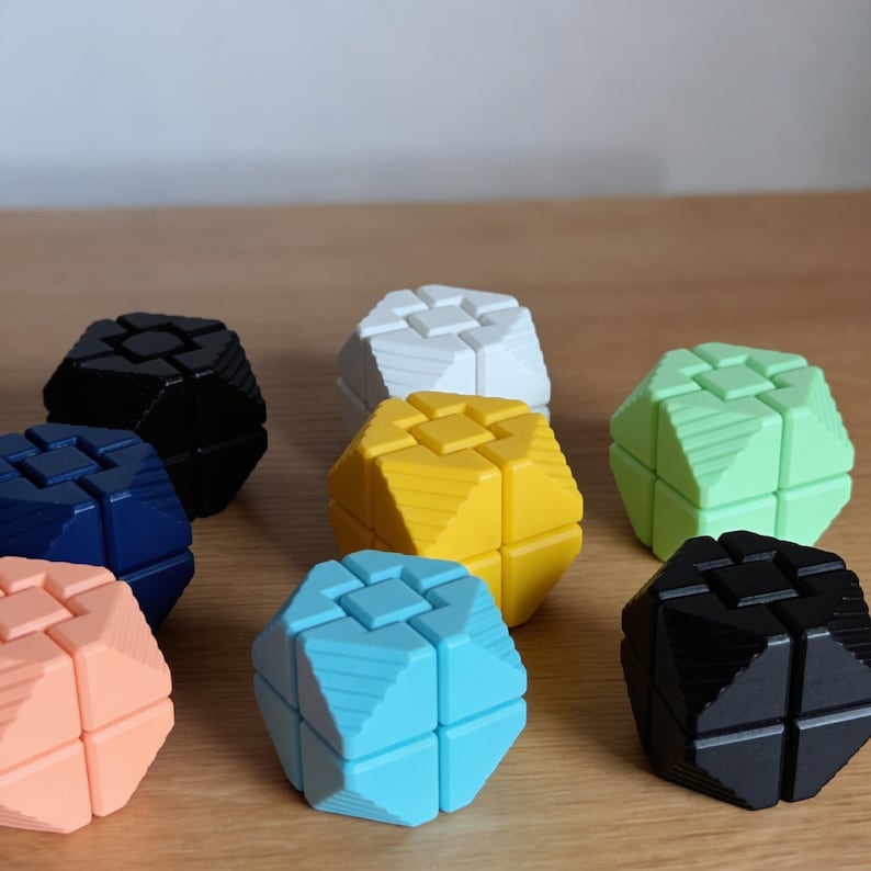 May include: A collection of colorful, geometric puzzle cubes in various colors, including black, white, yellow, blue, and green. Each cube has a unique design with interlocking pieces, suggesting a brain teaser or educational toy.