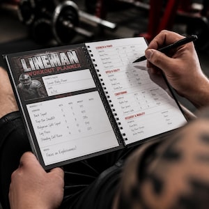 May include: A spiral-bound Lineman Workout Planner notebook with a black cover. The open pages feature printed sections for Strength and Power, Speed and Agility, Conditioning, and Recovery and Mobility, with handwritten workout logs.