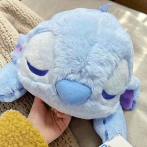 May include: A light blue plush toy shaped like a character with large ears, a blue nose, and closed eyes. The plush has a soft, fluffy texture and is in a sleeping pose. The toy is a popular character from a well-known animated film.