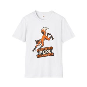May include: White t-shirt with a cartoon fox in orange, brown, and white. The fox is leaping, with the text "CERTIFIED FOX BEHAVIOR" in orange and black below. The shirt has a crew neck.