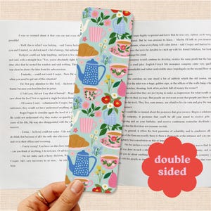 Op de afbeelding: Een rechthoekige boekenlegger met een lichtblauwe achtergrond met een herhalend patroon van theepotten, kopjes, schoteltjes, croissants, peren en diverse bloemen in roze, rode, gele en groene tinten. Een rood bloemvormig icoon vermeldt double sided.