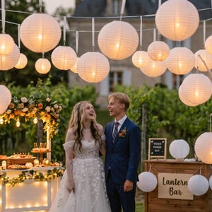Op de afbeelding: Een verzameling ronde witte papieren lantaarns die aan touwtjes boven een houten bar hangen met een bordje met de tekst Lantern Bar. De lantaarns zijn van binnenuit verlicht en werpen een warme gloed over de buitenomgeving.