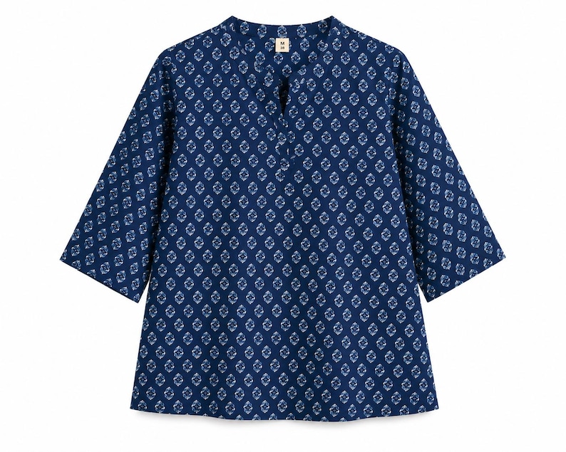 May include: A dark blue tunic with a repeating white diamond-shaped geometric pattern. The garment features three-quarter length sleeves, a split neckline, and a small white tag at the inner collar with the letter M printed in black.