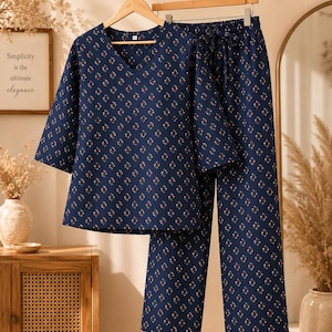 Könnte beinhalten: Ein marineblaues Pyjama-Set bestehend aus einem Oberteil mit V-Ausschnitt und Dreiviertelärmeln sowie einer passenden Hose mit weitem Bein und elastischem Kordelzugbund, verziert mit einem kleinen, sich wiederholenden floralen Muster.