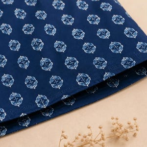 May include: A dark blue fabric featuring a repeating white botanical pattern of small, stylized leaves arranged in a symmetrical diamond-like formation. The material has a visible stitched hem along the bottom edge, showcasing a clean finish.