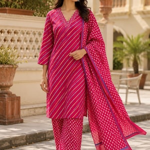 Puede incluir: Un conjunto de tres piezas en fucsia vibrante que consta de una túnica hasta la rodilla con rayas diagonales multicolores, pantalones anchos con un patrón de puntos blancos y un chal dupatta largo a juego con el mismo diseño.