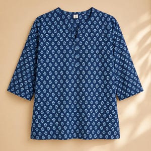 May include: A dark blue tunic with three-quarter length sleeves and a split V-neckline. The garment features an all-over repeating light blue floral block print pattern. A small white tag with the letter M is visible at the inner neckline.