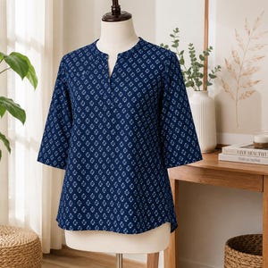 May include: A dark blue blouse featuring a repeating white geometric diamond pattern, three-quarter length sleeves, and a notched V-neckline. The garment is displayed on a mannequin, showcasing a straight hemline and a relaxed, comfortable fit.
