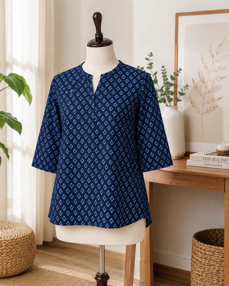 May include: A dark blue blouse featuring a repeating white geometric diamond pattern, three-quarter length sleeves, and a notched V-neckline. The garment is displayed on a mannequin, showcasing a straight hemline and a relaxed, comfortable fit.