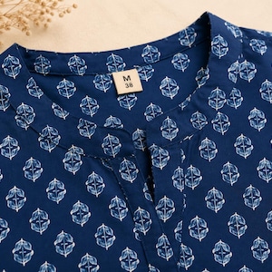 May include: A dark blue shirt featuring a repeating white botanical leaf pattern. The garment has a mandarin collar with a small front slit neckline. A rectangular tag inside the collar displays the text M 38, indicating the size of the shirt.