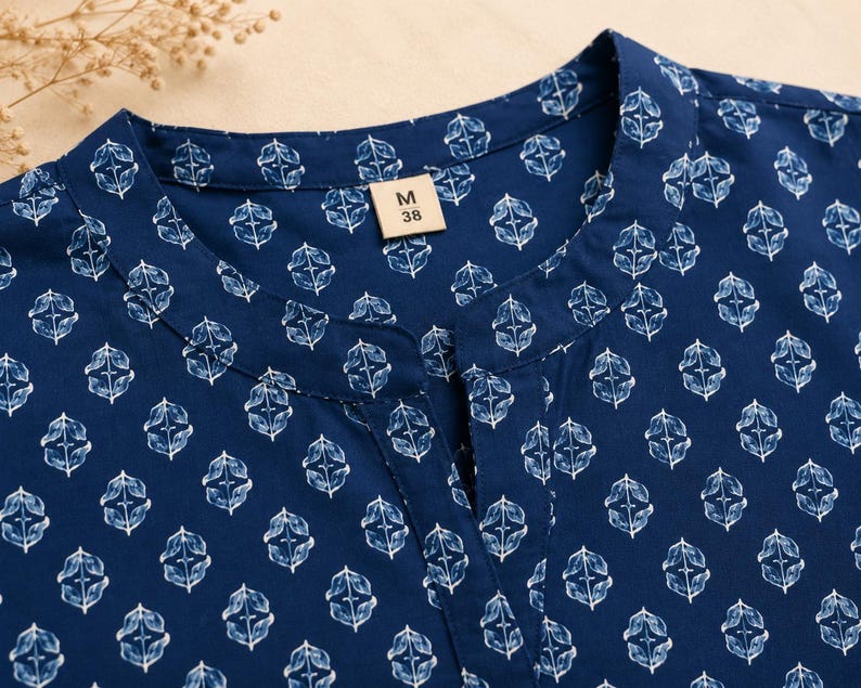 May include: A dark blue shirt featuring a repeating white botanical leaf pattern. The garment has a mandarin collar with a small front slit neckline. A rectangular tag inside the collar displays the text M 38, indicating the size of the shirt.