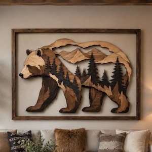 Könnte beinhalten: Große Wandkunst aus Holz mit einem Bären, der durch eine Waldszene läuft. Der Bär ist aus verschiedenen Brauntönen gefertigt, mit einer Berg- und Baumsilhouette im Hintergrund. Das Kunstwerk ist in dunklem Holz gerahmt.