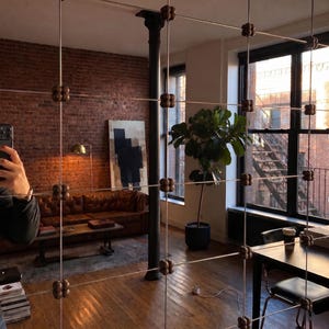 May include: A room divider screen featuring a grid of thin vertical and horizontal metal wires connected by small, dark brown, four-lobed wooden beads at each intersection, creating a structured, semi-transparent partition within a living space.
