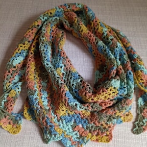Può includere: Uno scialle all'uncinetto fatto a mano e colorato, nei toni del blu, pesca, giallo e verde. Il design a trama aperta crea una sensazione leggera e ariosa. Lo scialle è piegato e drappeggiato, mostrando l'intricato lavoro a maglia.