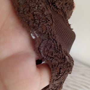 K&ouml;nnte beinhalten: Nahaufnahme eines braunen Kleidungsst&uuml;cks mit einem strukturierten, spitzenartigen Besatz. Der Stoff scheint ein dunkler Braunton zu sein, mit einem gerippten Abschnitt. Das Bild hebt die komplizierten Details des Textils hervor.