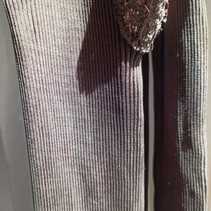 K&ouml;nnte beinhalten: Nahaufnahme eines dunkelbraunen Rippstrickkleidungsst&uuml;cks. Der Stoff hat vertikale Linien und eine strukturierte Oberfl&auml;che. Ein Teil eines braunen, offen gewebten Designs ist oben sichtbar, m&ouml;glicherweise ein &Auml;rmeldetail. Die Beleuchtung erzeugt Schatten.