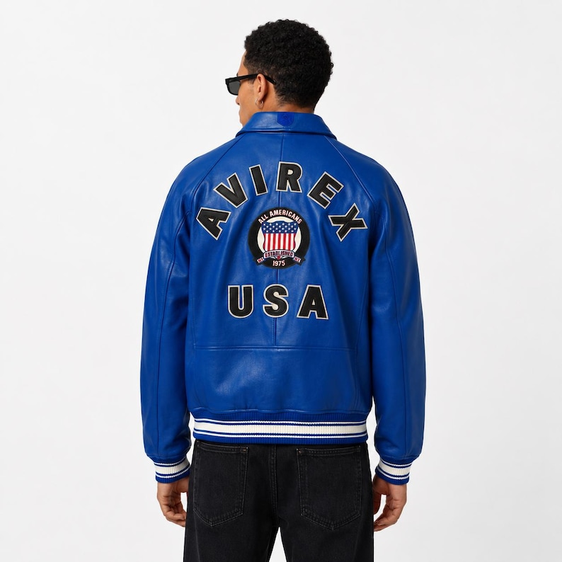 May include: A vibrant blue leather jacket with the word "AVIREX" arched across the back, above a circular patch with the words "All Americans" and "USA". The jacket has a ribbed hem and cuffs with white stripes.