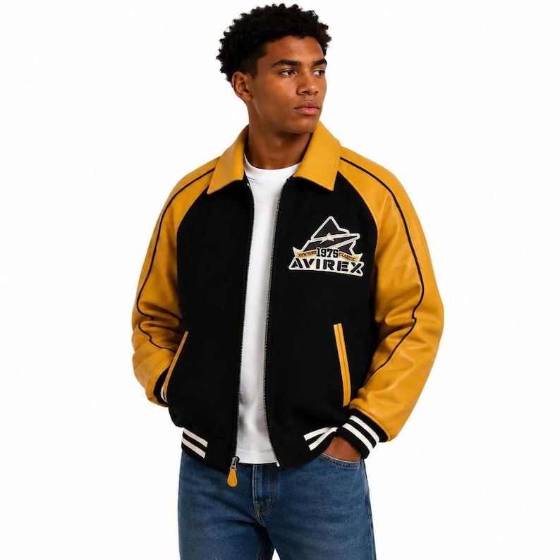 May include: Black and gold varsity jacket with the text "AVIREX 1975" on the chest. The jacket features a black body, gold sleeves, collar, and pocket trim, and white stripes on the cuffs and hem. A classic bomber jacket style.