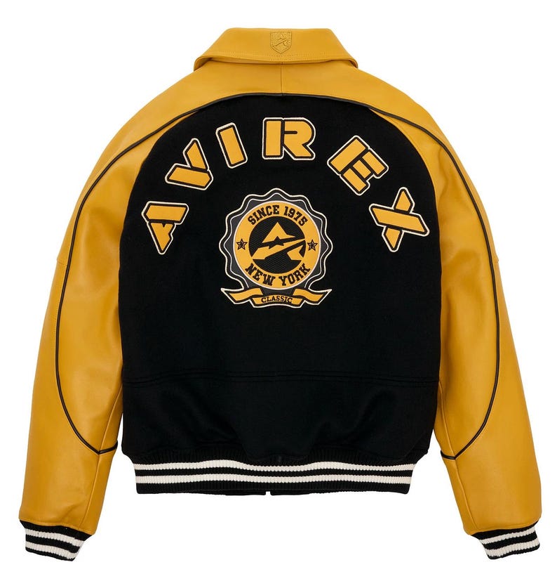May include: A varsity-style jacket with a black body and mustard yellow leather sleeves. The back features the word "AVIREX" and a circular emblem with "SINCE 1975 NEW YORK CLASSIC" text. The jacket has a collar and striped cuffs.