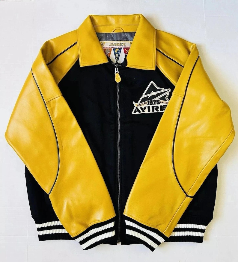 May include: A black and yellow jacket with a zip-up front. The jacket has yellow leather sleeves and collar, with black fabric on the body. The jacket has the text "AVIREX NEW YORK 1975 CLASSIC" on the chest and white stripes on the cuffs.