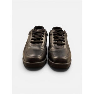 May include: A pair of black leather sneakers with black laces. The shoes have a rounded toe and a thick sole. The sneakers are displayed on a white background.
