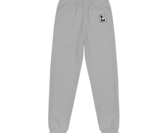 May include: Light grey sweatpants featuring an elastic waistband and cuffed ankles. On the upper right thigh, there is a small, square black and white patch displaying a stylised maple leaf icon inside a rectangular border.