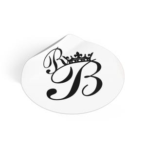 Puede incluir: Una pegatina blanca con un diseño negro. El diseño presenta las letras "R" y "B" entrelazadas, coronadas con una corona. La pegatina tiene una forma redondeada con una ligera curva en la parte superior.