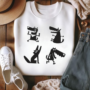 Pode incluir: Camisola branca com quatro ilustrações de lobos pretos de desenho animado em poses diferentes. A camisola tem gola redonda e mangas compridas. O design está centrado na frente.