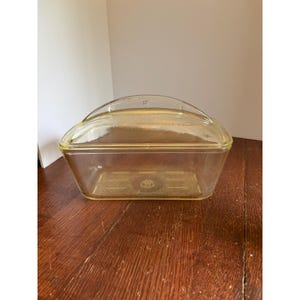 Peut inclure: Un beurrier rectangulaire en verre jaune transparent avec un couvercle assorti. Le couvercle présente une poignée incurvée et la base comporte un logo W moulé au centre du fond. Le verre a une finition lisse et polie sur toute la pièce.