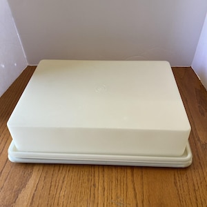 Peut inclure: Un récipient en plastique blanc cassé de forme rectangulaire avec un couvercle assorti. Le récipient repose sur une base légèrement plus grande. Le couvercle comporte une petite indentation circulaire au centre. Le récipient est probablement destiné au stockage des aliments.