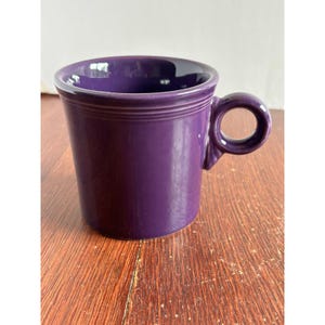 May include: A deep purple ceramic mug with a glossy finish, featuring a cylindrical body, a wide circular handle, and three distinct horizontal embossed rings circling the upper portion of the exterior wall just below the rim.