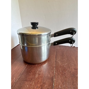 May include: A stainless steel double boiler set featuring a polished silver finish, two black heat-resistant handles with integrated metal hanging loops, and a matching lid with a small black knob centred on top for easy lifting and handling.