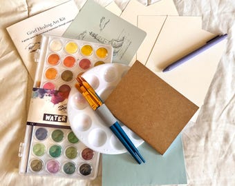May include: A Grief Healing Art Kit with watercolor paints, paintbrushes, a palette, and blank cards. The kit includes a booklet with the text "Grief Healing Art Kit" and a pen. The watercolor paints are in a clear plastic case.