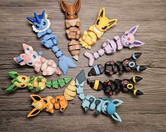 May include: A collection of ten articulated plastic figures representing various fictional creatures in different colors including brown, blue, yellow, pink, green, orange, purple, and black, arranged in a circular pattern on a wood grain surface.