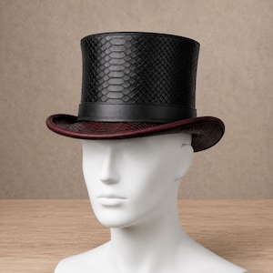 Peut inclure: Un haut-de-forme doté d'une calotte à texture de peau de serpent noire et d'un bord à texture de peau de serpent bordeaux foncé. Le chapeau comprend une bande en cuir noir lisse entourant la base de la calotte, créant un contraste net.