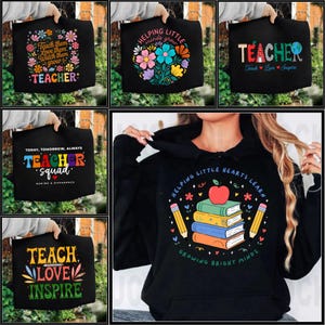 Op de afbeelding: Zwarte hoodies met kleurrijke ontwerpen en tekst. Eén zegt "TEACHER" met bloemen, een andere "HELPING LITTLE minds grow", en een derde "TEACHER Teach Love Inspire". Andere hoodies zeggen "TEACHER squad" en "TEACH LOVE INSPIRE".