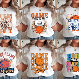 Può includere: Magliette bianche con grafiche a tema basket. I disegni includono palloni da basket, canestri e frasi come "My Heart is on That Court", "Game Day Y'all" e "Courtside Cutie Energy". Sono abbigliamento casual.