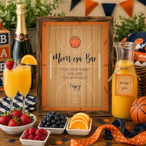 May include: A framed sign with a basketball court graphic and the text Mom-osa Bar, Pour Some Bubbly, Add Juice, Top With Fruit, Enjoy. The sign is surrounded by two glasses of orange juice with strawberries, a carafe of orange juice, and bowls of fruit.