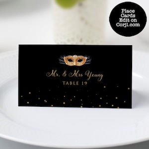 Peut inclure: Carte de place noire avec du texte doré et un motif de masque de mascarade doré. La carte indique "Mr. & Mrs. Young" et "Table 19". La carte a des accents de paillettes dorées et le texte "Place Cards Edit on Corjl.com" dans un cercle noir.