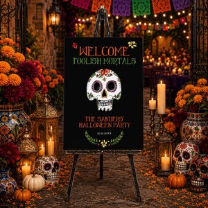 May include: A black rectangular sign on a tripod stand featuring a white sugar skull illustration, orange and green text reading WELCOME FOOLISH MORTALS, THE SANDERS' HALLOWEEN PARTY, and 10.31.20XX, accented with green leaf and yellow flower graphics.