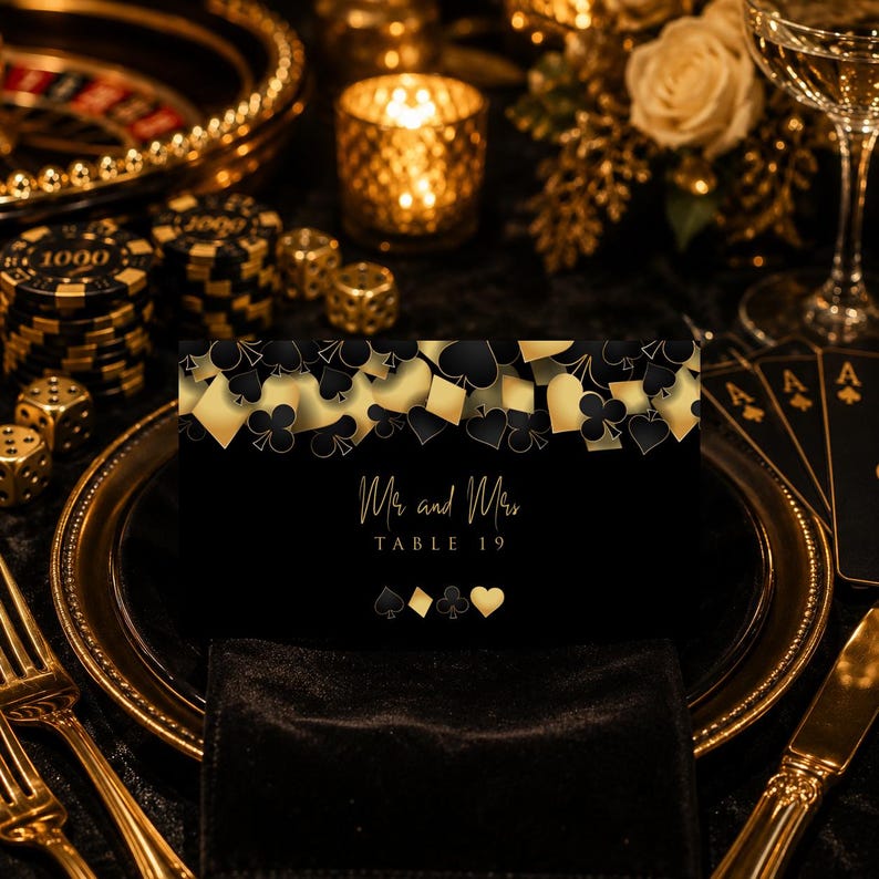 May include: A black rectangular table card featuring a gold and black playing card suit pattern at the top. The text reads Mr and Mrs TABLE 19 in gold script and serif font, with gold spade, diamond, club, and heart icons centred below.
