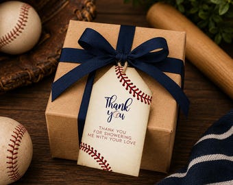 Peut inclure: Une boîte cadeau carrée en carton brun nouée avec un ruban bleu foncé et une étiquette crème. L'étiquette présente des graphismes de coutures de baseball rouges, le texte "Thank you" et "THANK YOU FOR SHOWERING ME WITH YOUR LOVE" en bleu.