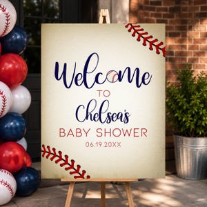 May include: A baseball-themed welcome sign on a wooden easel. The sign reads "Welcome to Chelsea's Baby Shower" in navy blue script, with a baseball graphic. Red baseball stitching accents the corners. Balloons in red, white, and blue are visible.